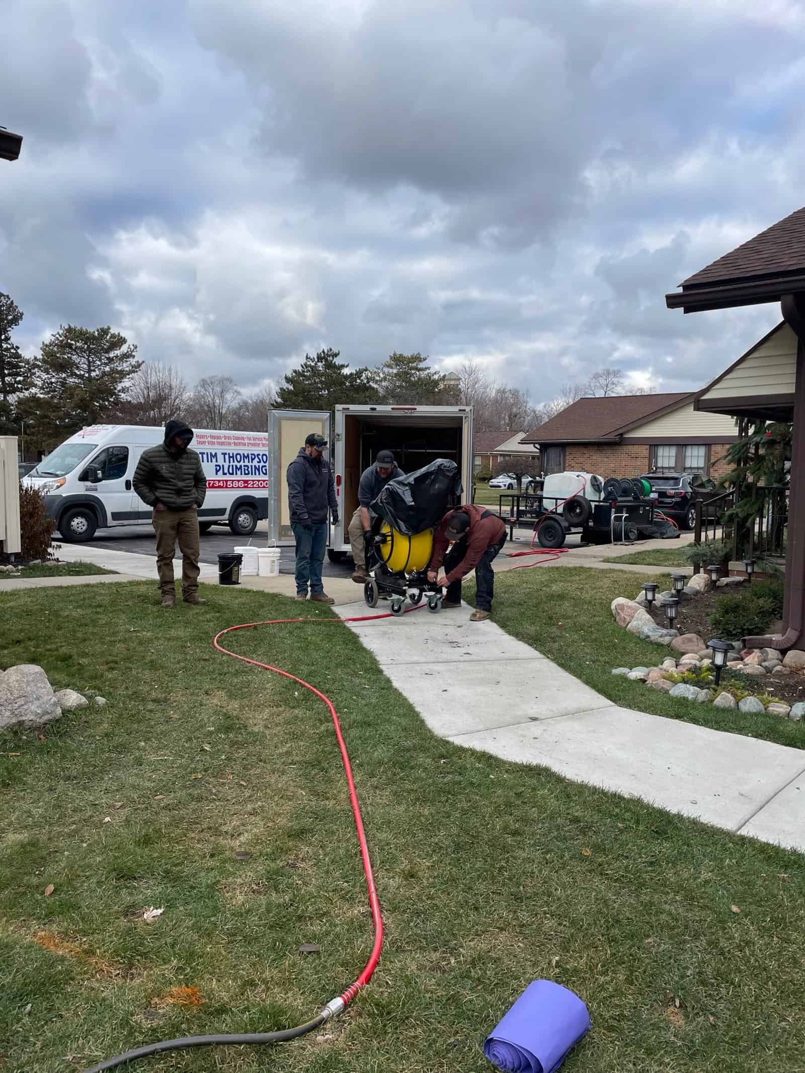 Workers fix a home's sewer line as a Thompson Trenchless and Hydro Jetting van is parked nearby on the street.