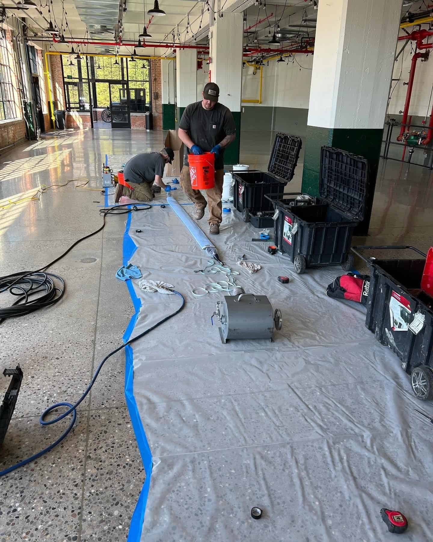 Thompson Trenchless and Hydro Jetting workers prepare drain cleaning equipment for a plumbing job in a spacious work area.