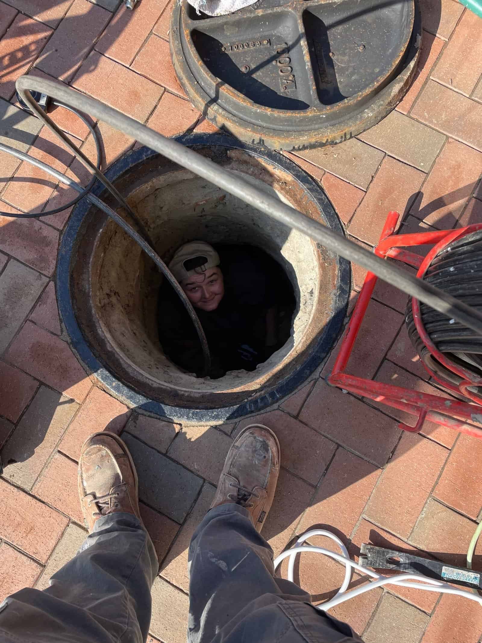 Thompson Trenchless and Hydro Jetting team uses special tools to clear pipes while working at a manhole.