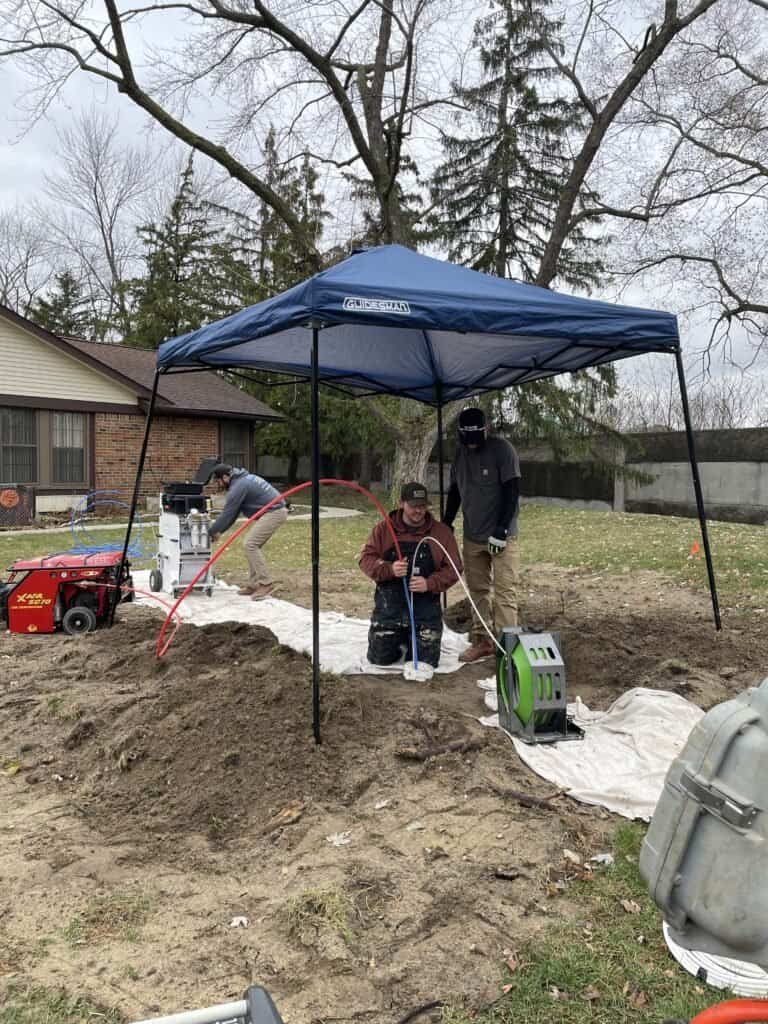 Thompson Trenchless and Hydro Jetting staff inspects and repairs yard pipes, showing teamwork and expert service on site.