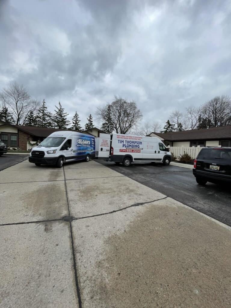 Two home service vans, including Thompson Trenchless and Hydro Jetting, are ready for pipe repair jobs in a neighborhood.