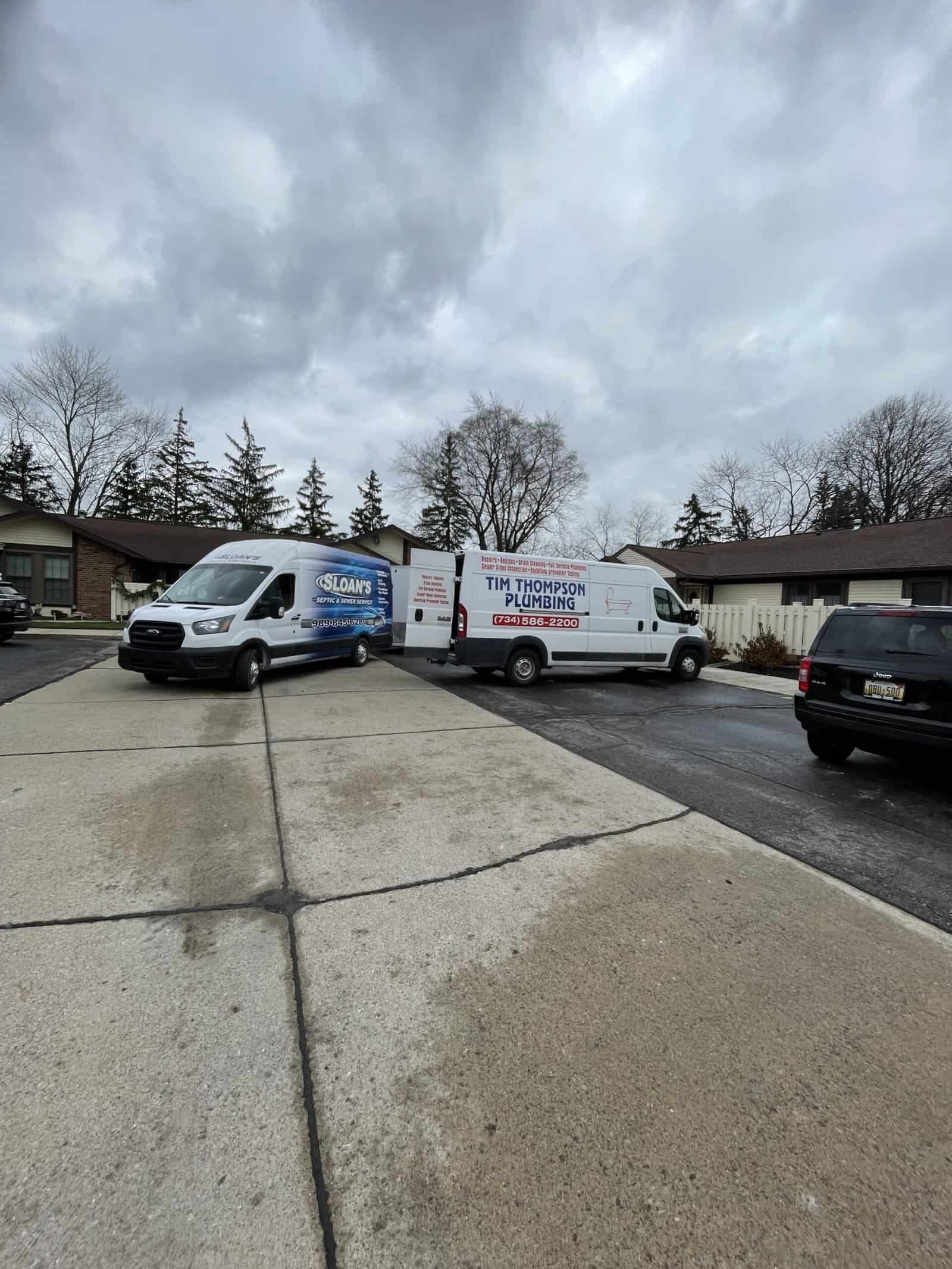 Two home service vans, including Thompson Trenchless and Hydro Jetting, are ready for pipe repair jobs in a neighborhood.
