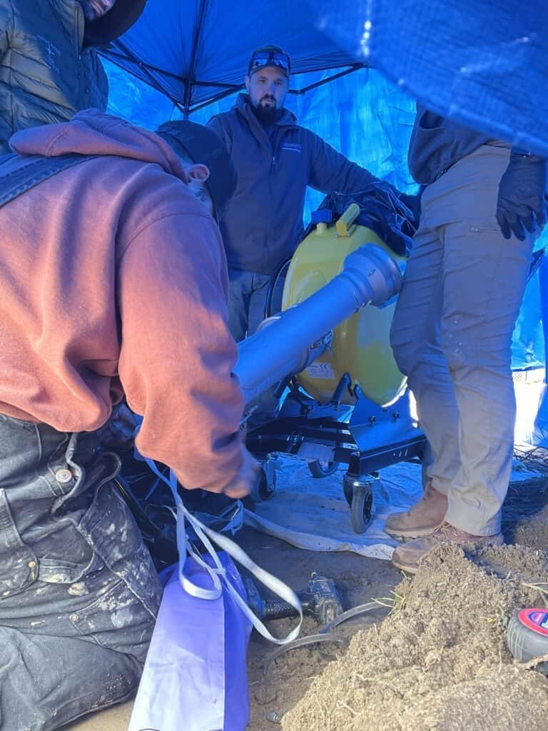 Thompson Trenchless and Hydro Jetting crew uses special equipment in a tent to fix pipes at a construction site.