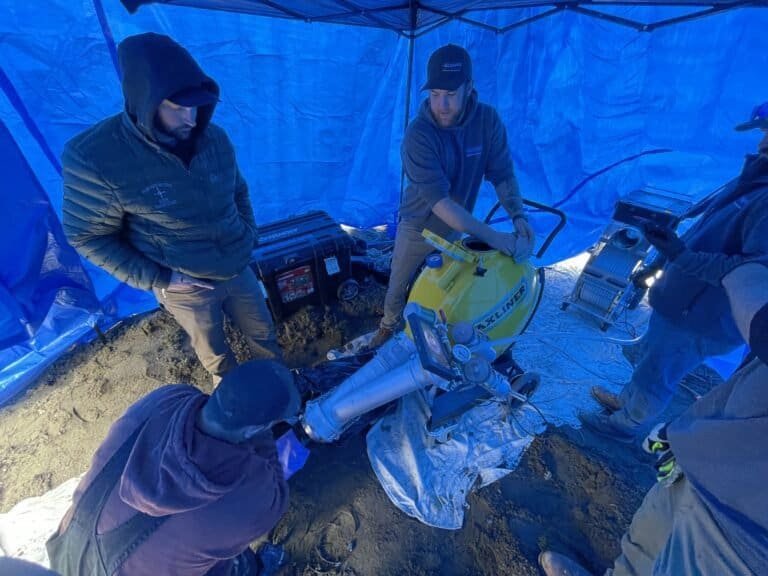 Thompson Trenchless and Hydro Jetting team uses tools to inspect pipes, showing skill and teamwork on a plumbing job.