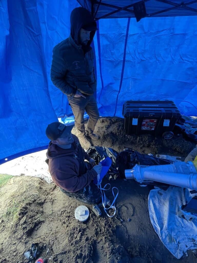 Thompson Trenchless and Hydro Jetting team checks pipes, working together to fix sewer lines in a tented area.