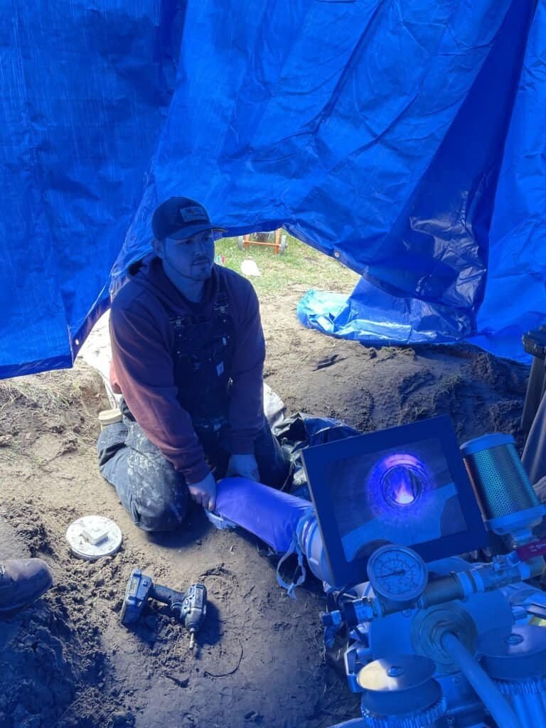 A Thompson Trenchless and Hydro Jetting worker checks pipe equipment during a service using advanced technology.