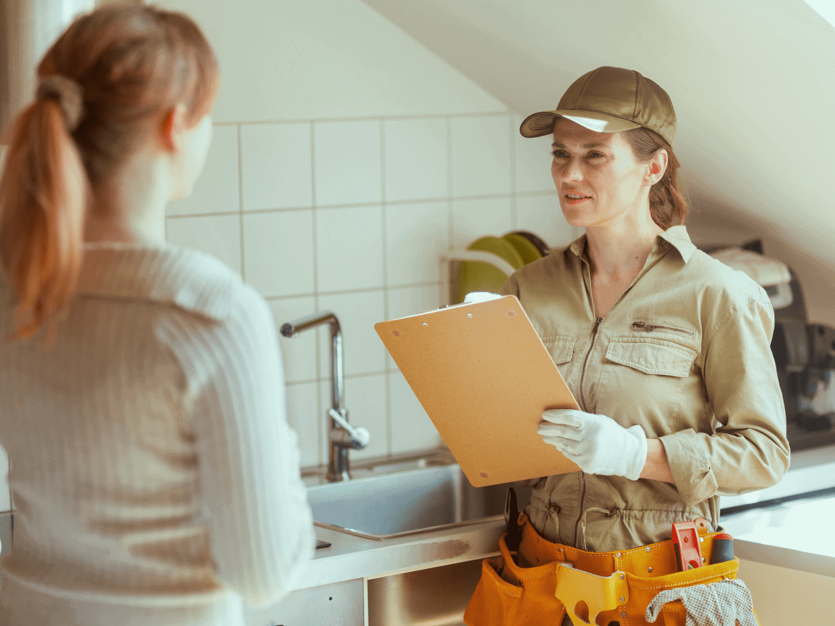 A Thompson Trenchless and Hydro Jetting worker talks with a customer in a kitchen about a pipe inspection service.