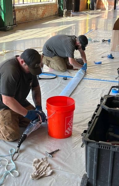 Thompson Trenchless and Hydro Jetting workers repair sewer lines indoors, showing skilled teamwork and safe work practices.