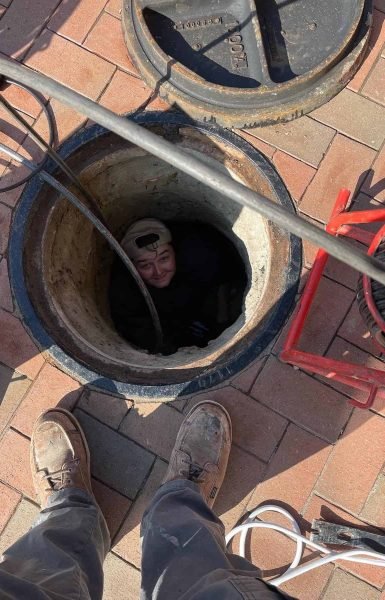 A Thompson Trenchless and Hydro Jetting worker inspects pipes in a manhole while another team member assists above.