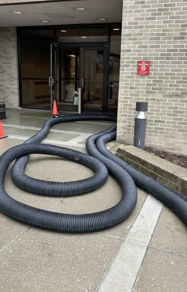 Thompson Trenchless and Hydro Jetting is repairing pipes at a building, with safety cones set up for the work area.