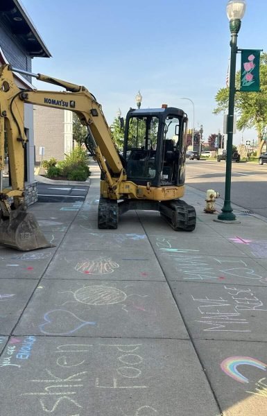 A yellow excavator and a Thompson Trenchless and Hydro Jetting banner promote services on a busy, welcoming street.